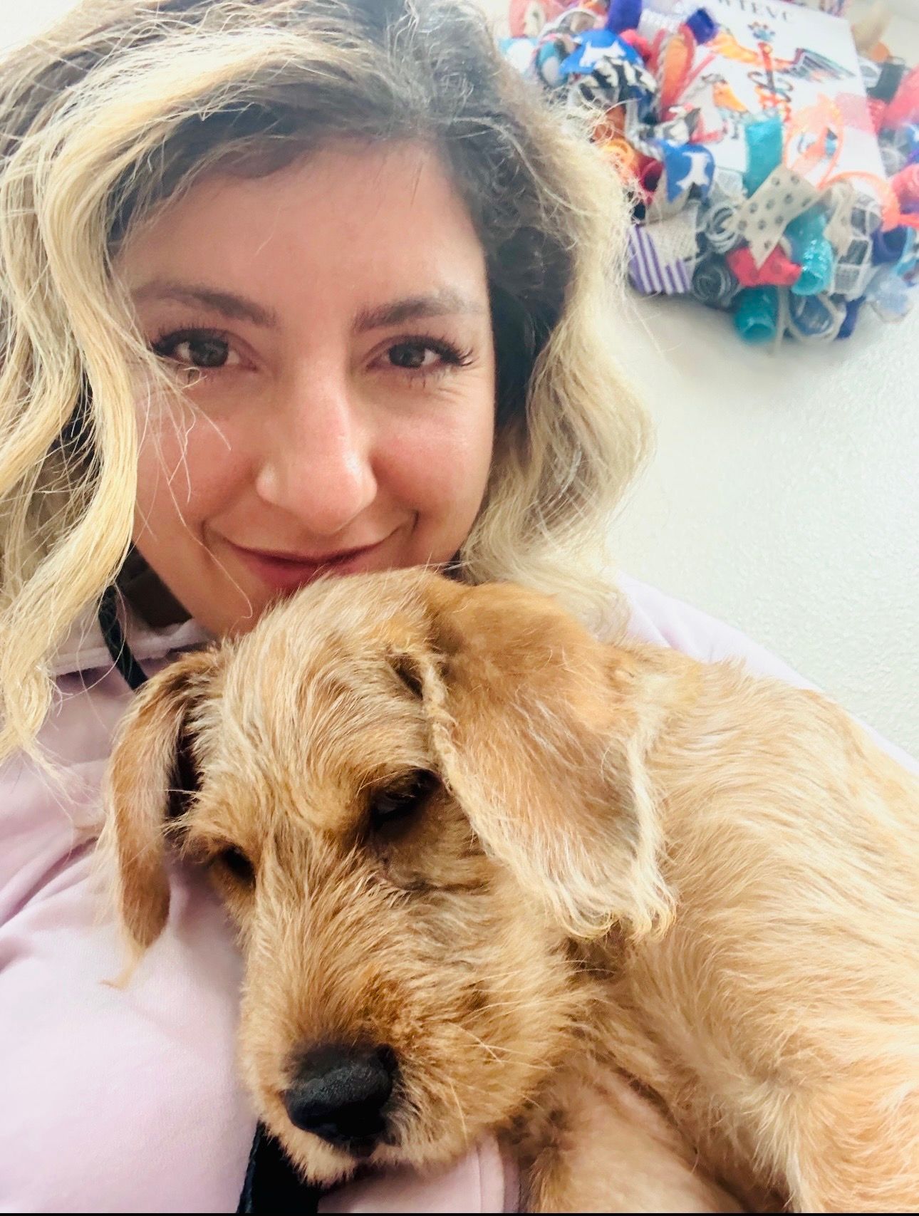 Woman holding a light brown dog, both looking at the camera.