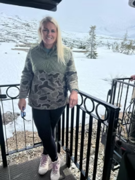 Woman in camouflage sweatshirt and leggings on a train, snowy mountain backdrop.