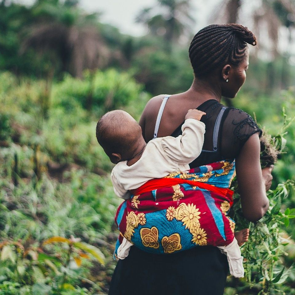 Photo of an African mother carrying her child on her back whilst harvesting food