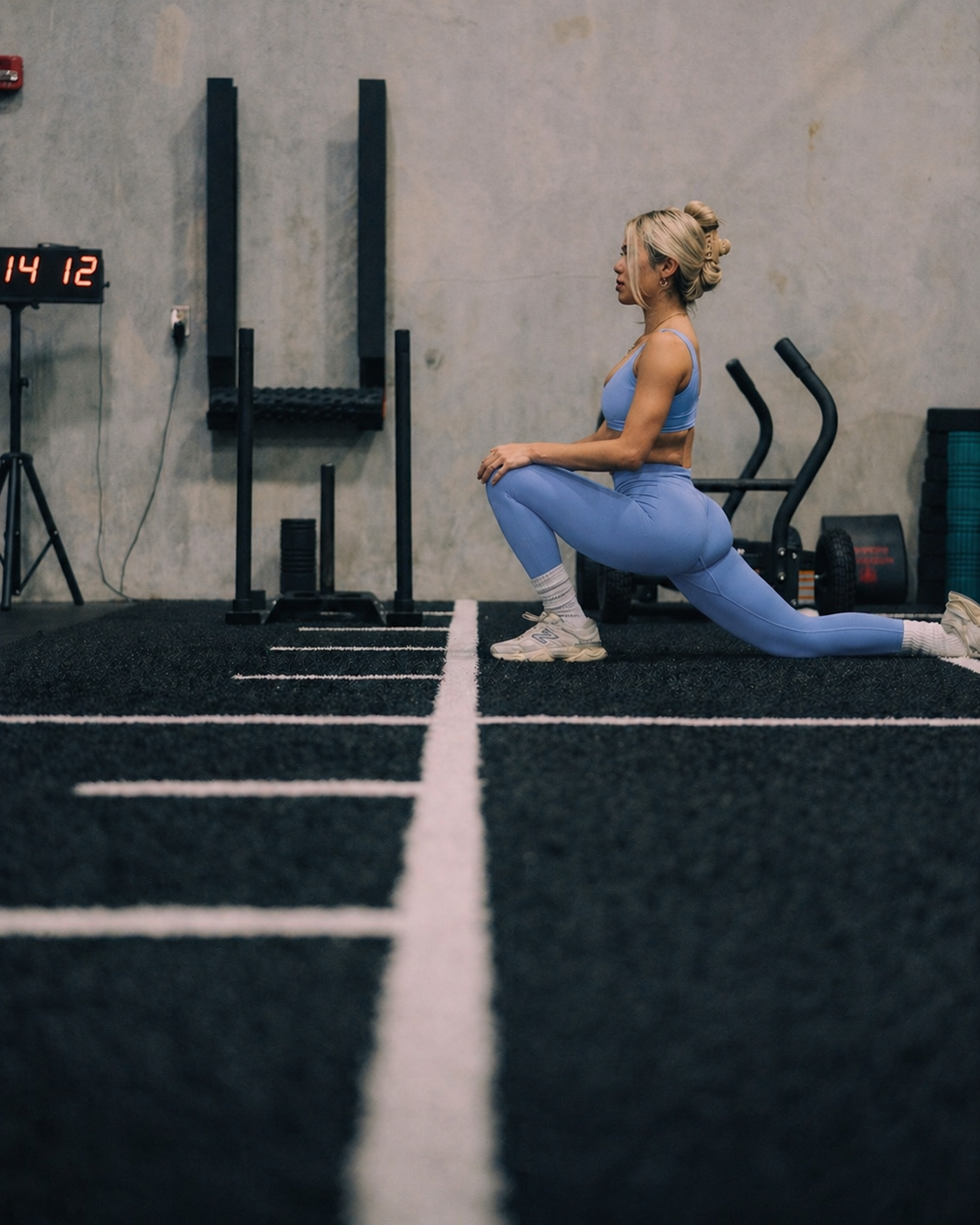 Woman in a gym doing a dumbbell row, dark setting, weights rack, bent over, holding a weight.
