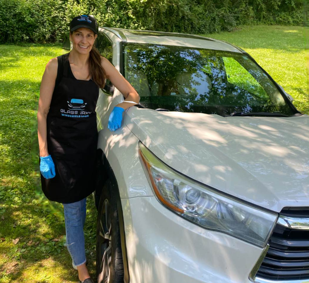 A woman in a black apron is standing next to a white car.