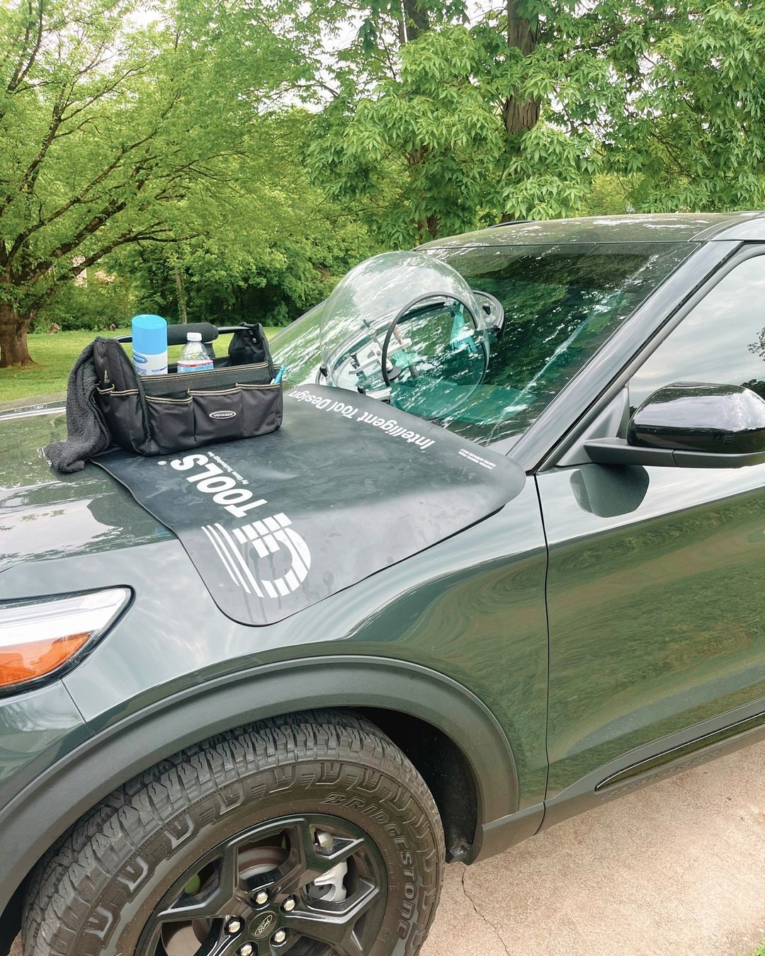 A green suv with a toolbox on the hood is parked in a driveway.