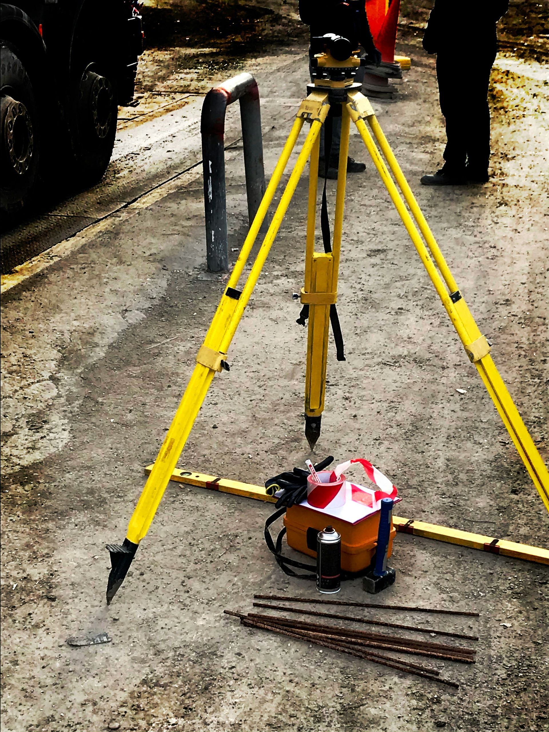 Surveying tripod and measuring tools on a wet roadside beside parked vehicles