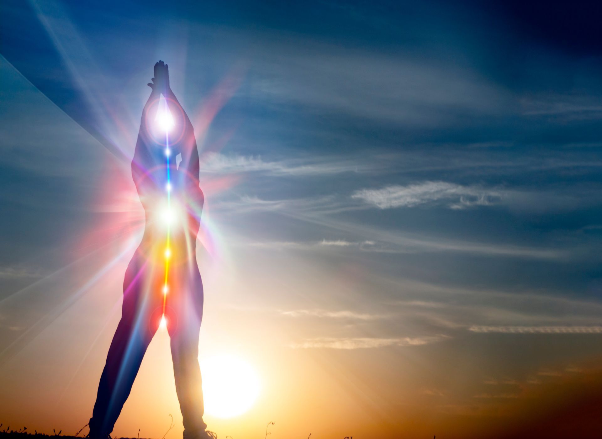 A person is standing in front of a sunset with their chakras glowing.