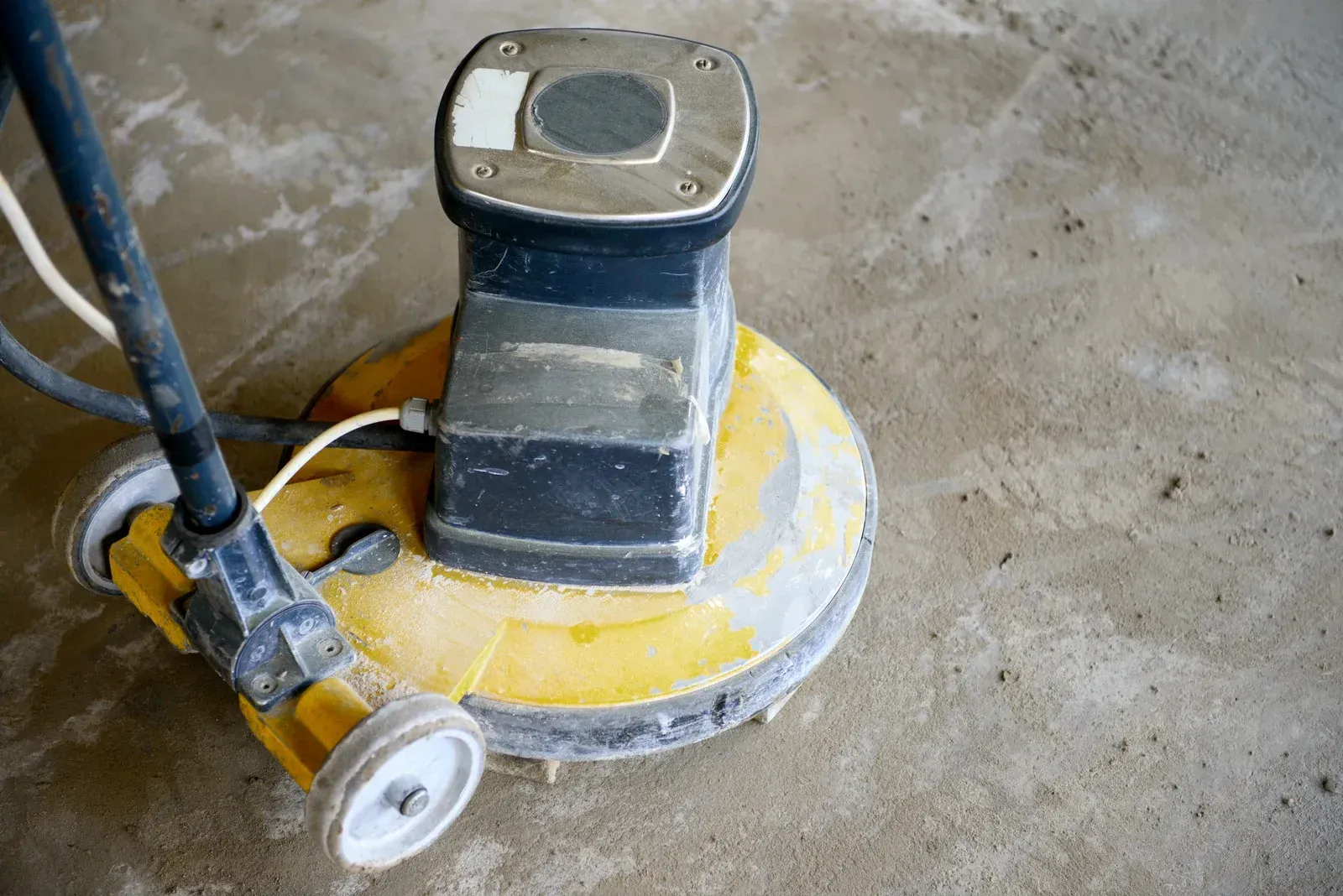A yellow industrial floor sander on a concrete surface, viewed from a high angle.