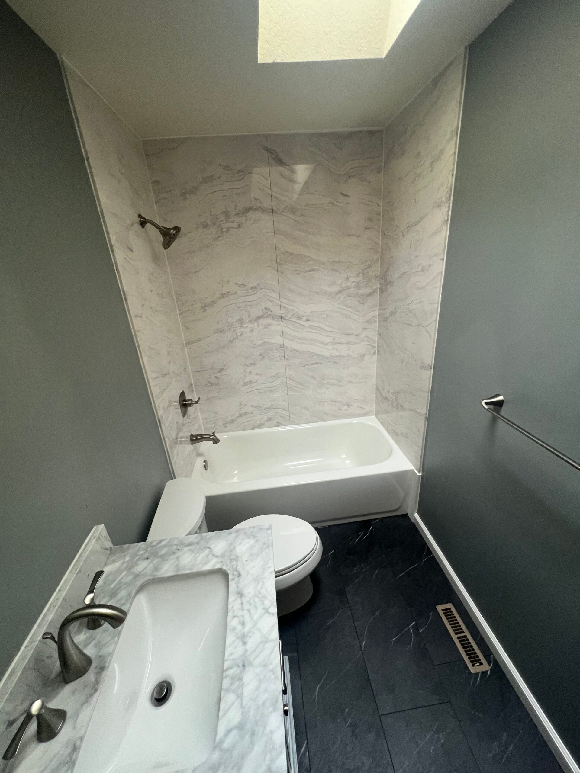 Small bathroom with white tub, sink, toilet, dark floor, and unfinished back wall.