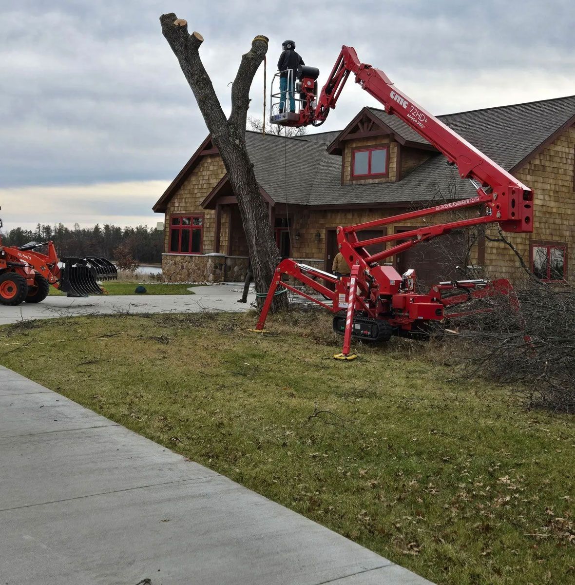 A red crane is cutting a tree in front of a house.