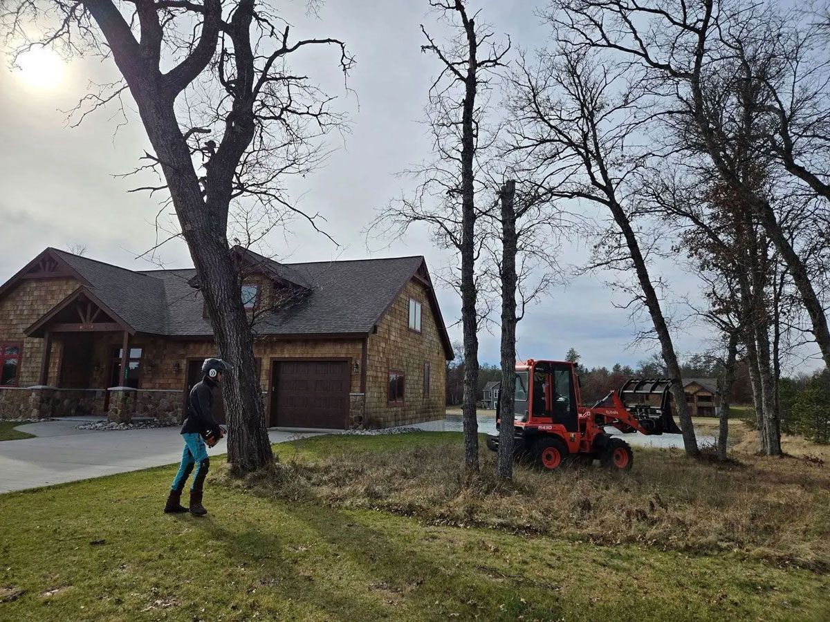 A woman is standing in front of a house with a tractor in the background.