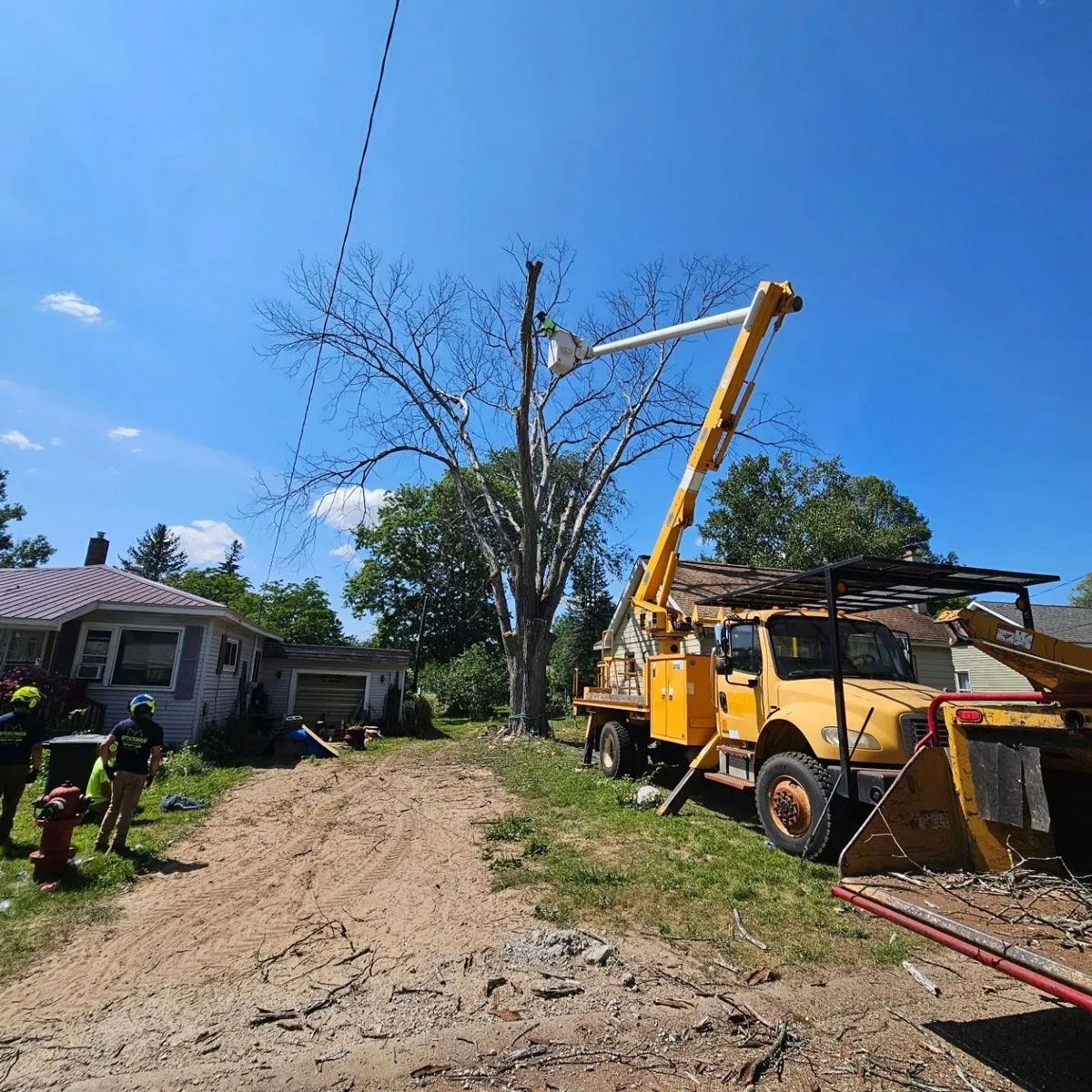 A yellow truck with a crane on top of it is parked in front of a house.