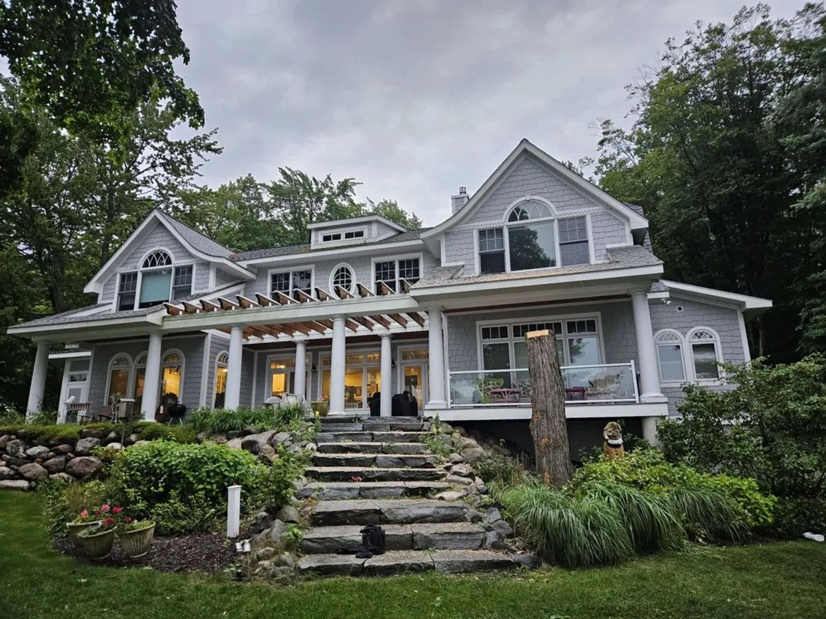 A large house with stairs leading up to it is surrounded by trees.