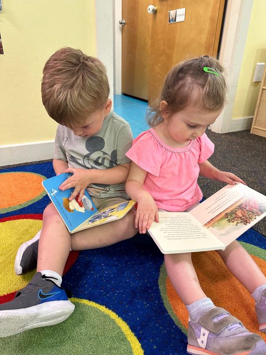 A boy and a girl are sitting on the floor reading books. | Brookline, NH | Scribbles Early Learning