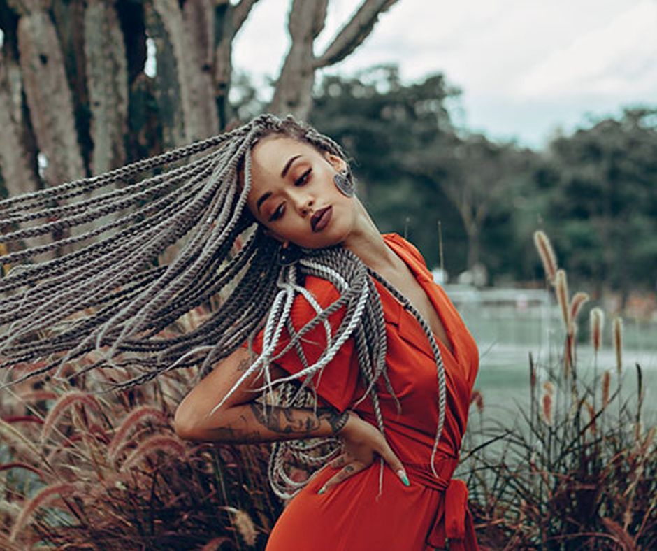 A Woman In A Red Dress With Braids In Her Hair Is Standing In Front Of A Tree