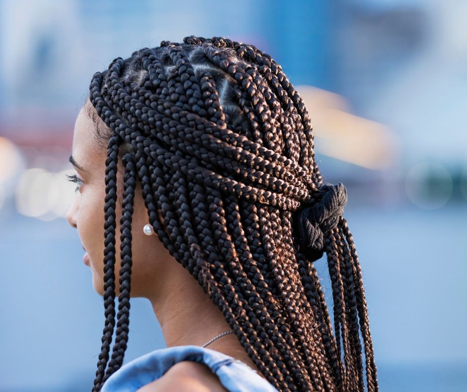 A Woman With Braids In Her Hair Is Standing In Front Of A City