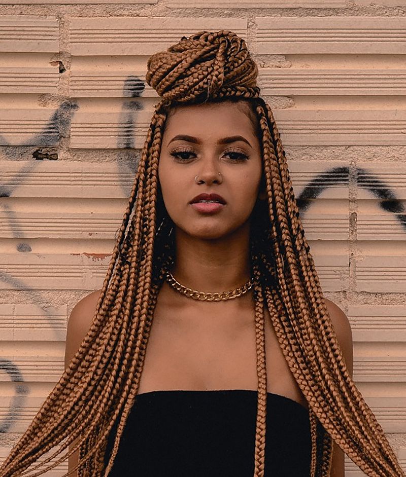 A Woman With Braids Is Standing In Front Of A Brick Wall