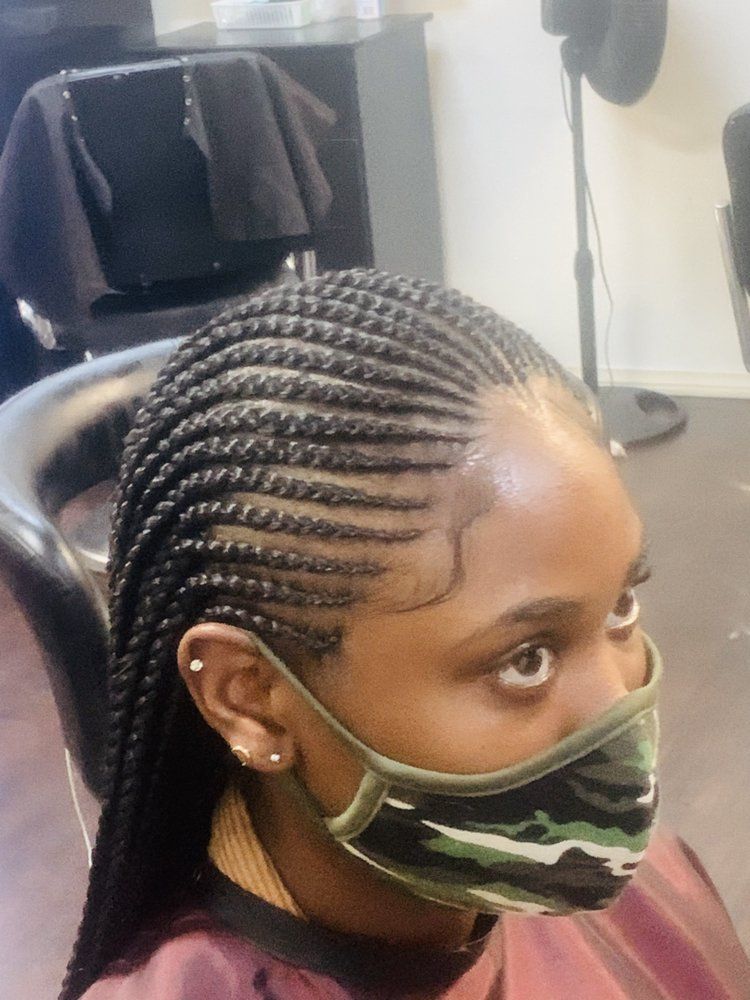 A Woman Wearing A Mask And Braids Is Sitting In A Chair