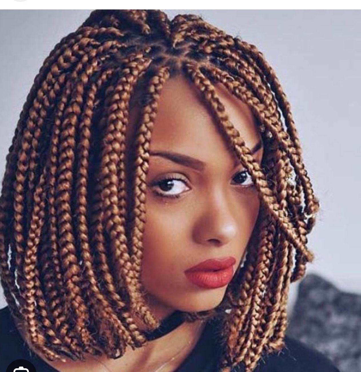 Woman with box braids, hand in hair, wearing gold jewelry, and a blue top.