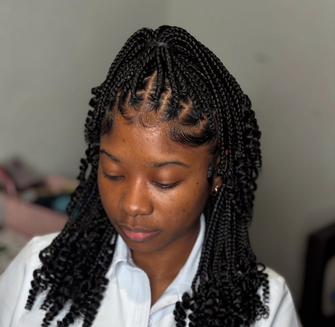 Woman with box braids and curly ends, looking down. Braids on top, loose curls frame her face.