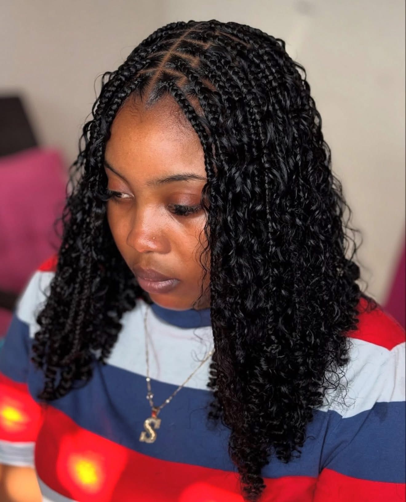 Woman with box braids and curly ends, wearing a striped shirt and necklace, looking down.