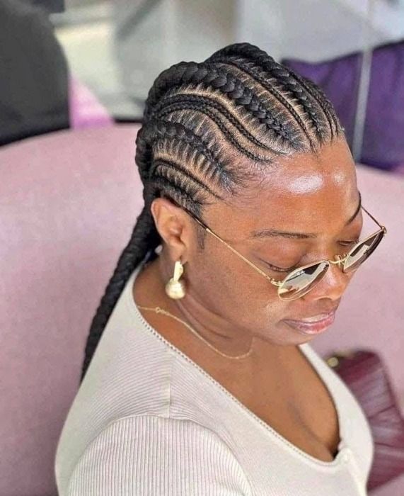 Woman with braided hairstyle, wearing sunglasses and light-colored top.