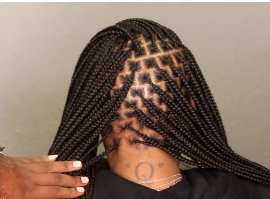 Box braids with a geometric pattern at the crown, held by a hand; close up.