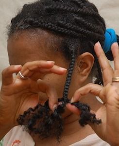 Woman twisting strands of black hair. Close-up view, indoor setting, hands in focus.