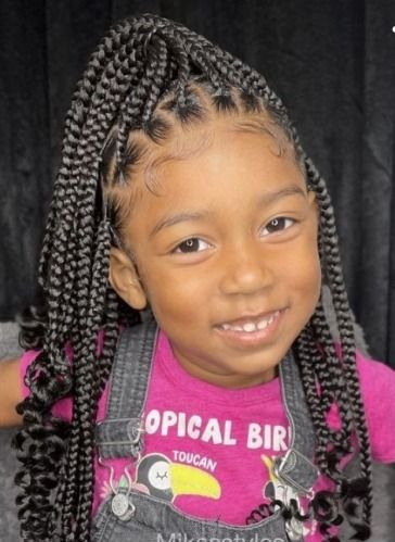 Girl with braided hair in high ponytail, wearing a pink shirt and denim overalls, smiling.