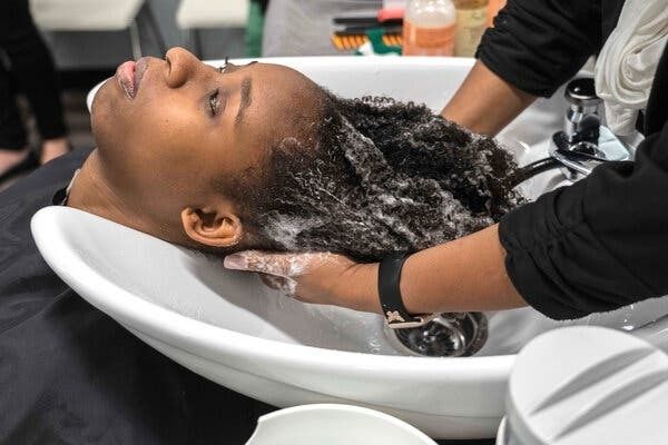 Person getting hair washed at a salon; head in a white basin, hands lathering hair.