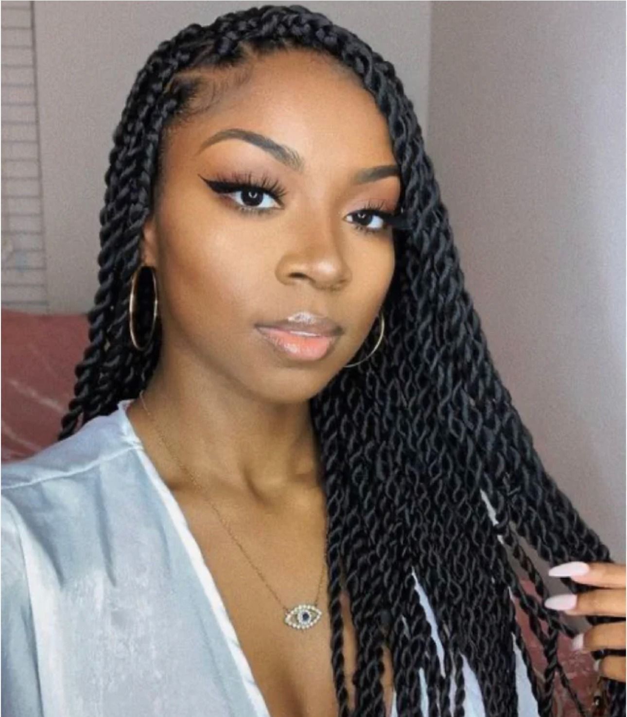 Woman with long black twists, wearing gold hoop earrings and a necklace, looking at the camera.
