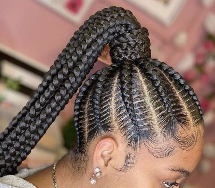 Person with cornrow braids wearing an earbud. Someone's hand is near the head, likely adjusting the hair.