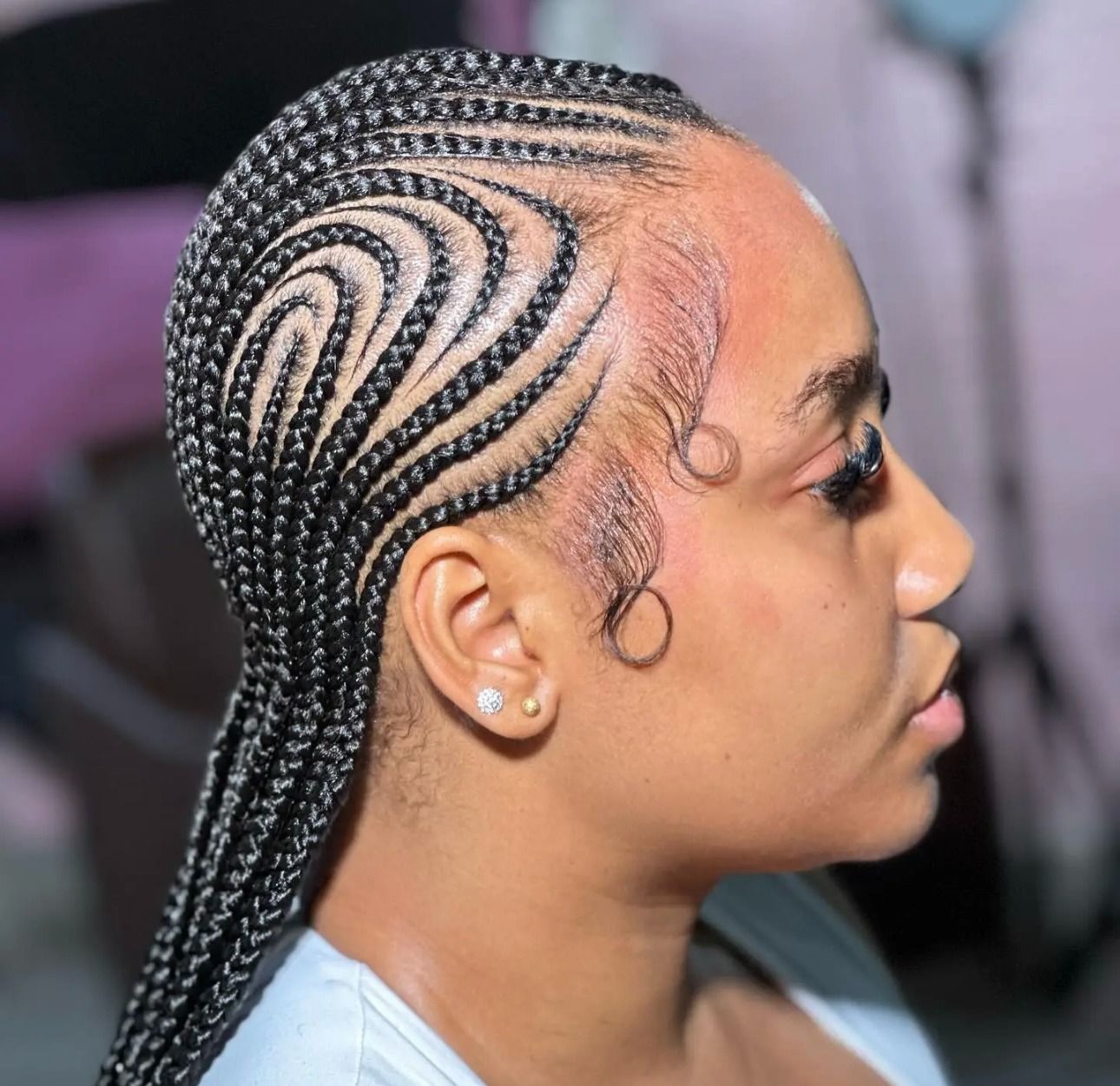 Braided hairstyle with swirling patterns; a person's profile is visible, showing neatly styled braids and baby hairs.