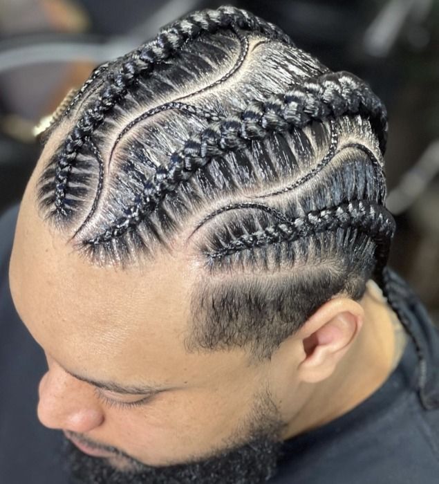 Man with black cornrows styled in curved, braided patterns. Short beard and faded haircut.