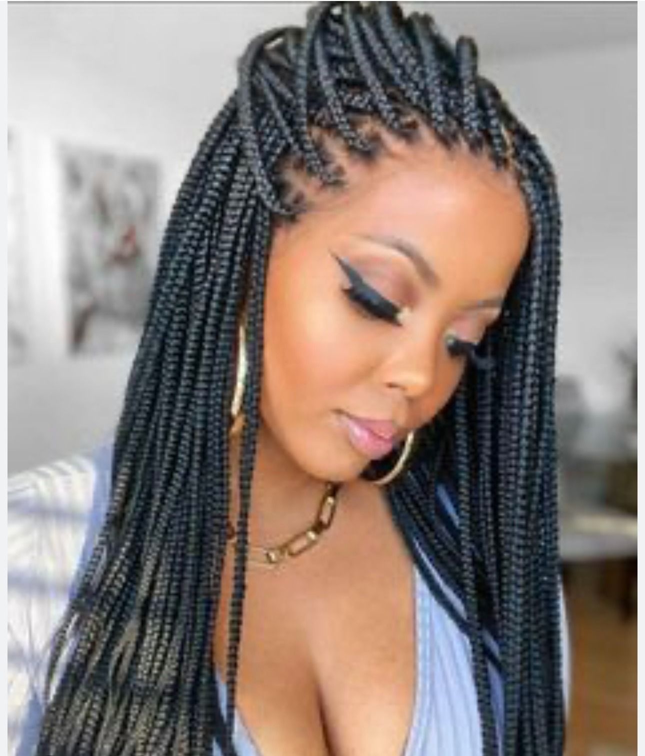Woman with box braids, hand in hair, wearing gold jewelry, and a blue top.