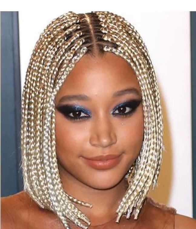 Woman with box braids, hand in hair, wearing gold jewelry, and a blue top.