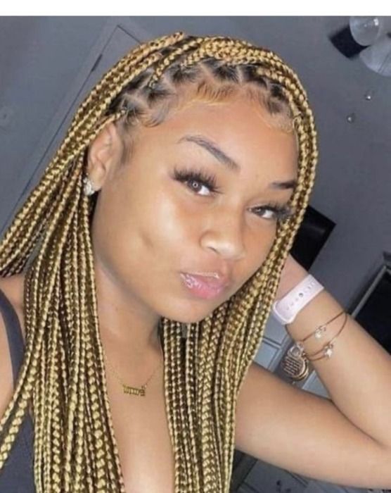 Woman with blonde box braids, wearing a necklace and a watch. She's looking towards the camera with a slight smile.