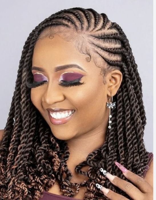Woman with braided hair smiling, wearing dangling earrings and makeup, close-up shot.