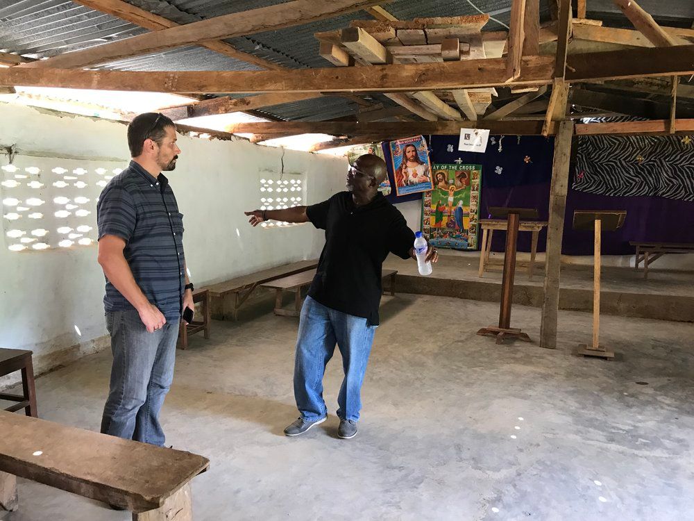Two men are standing in an empty room talking to each other.