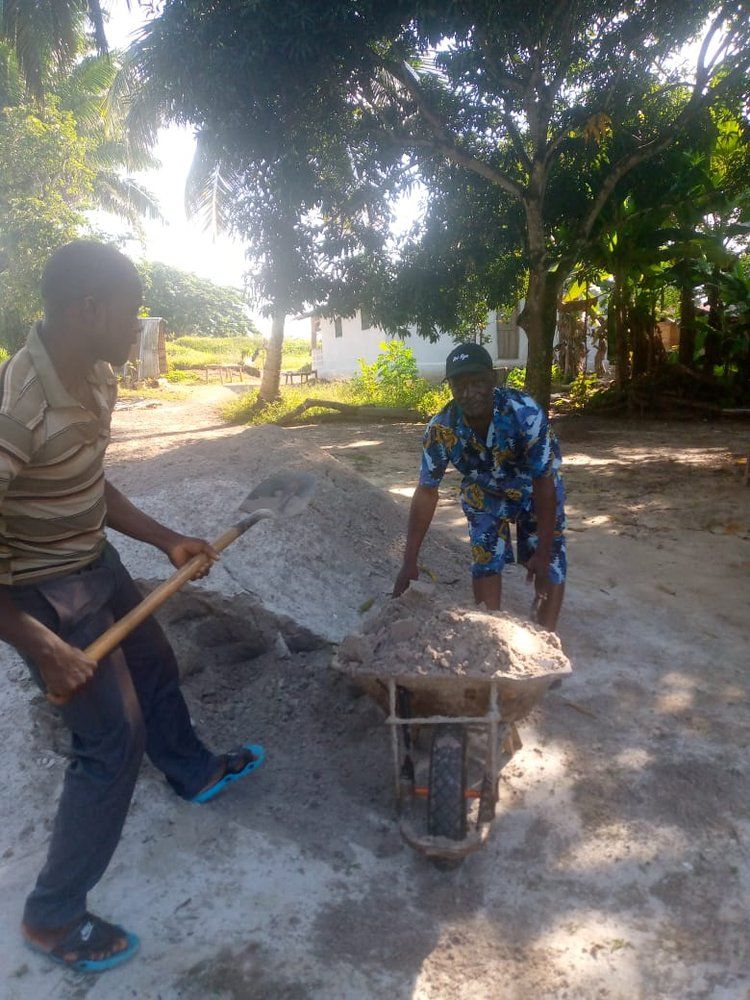 A man is pushing a wheelbarrow full of dirt while another man holds a shovel.