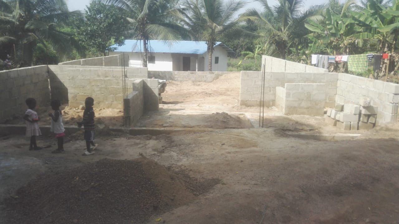Two children are standing in a dirt field in front of a building under construction.