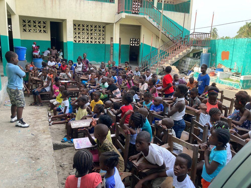 A group of children are sitting at tables outside of a building.