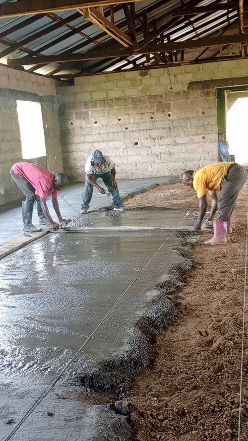 Three men are working on a concrete floor in a room.