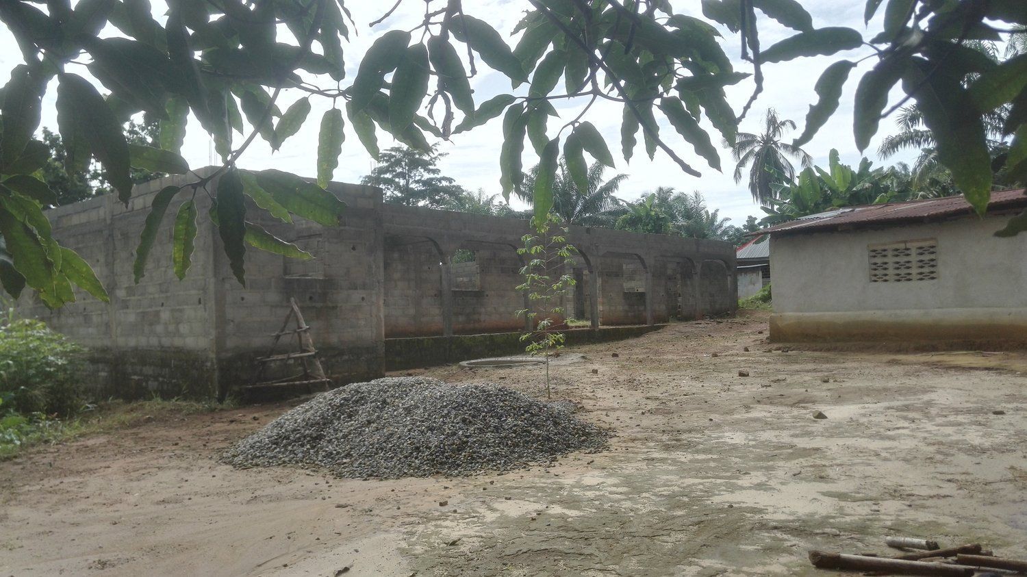 A pile of gravel is in the middle of a dirt field in front of a building.