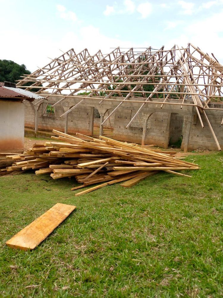 A pile of wood is sitting in the grass in front of a building under construction.