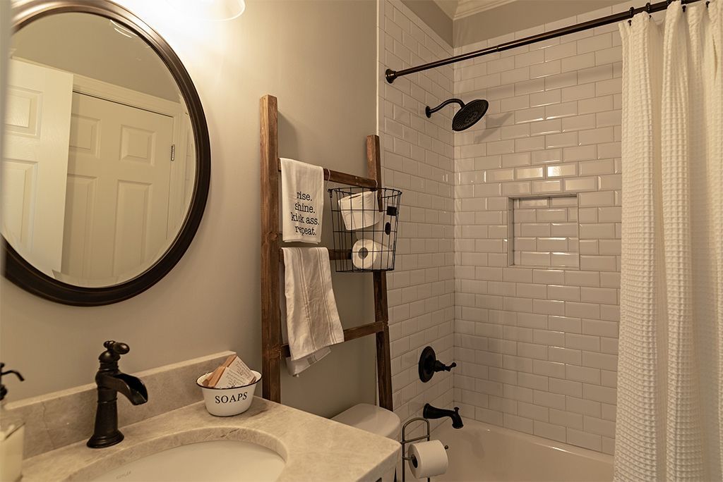 Bathroom with white subway tile shower, brown fixtures, and a wooden ladder for towels.