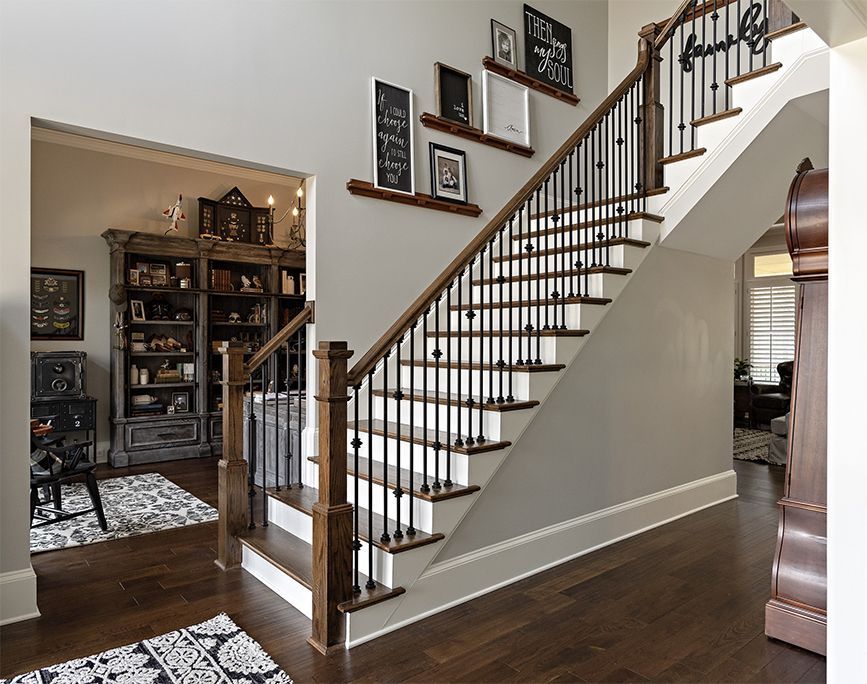 Staircase with wooden handrails and black iron balusters, ascending against a gray wall with artwork.