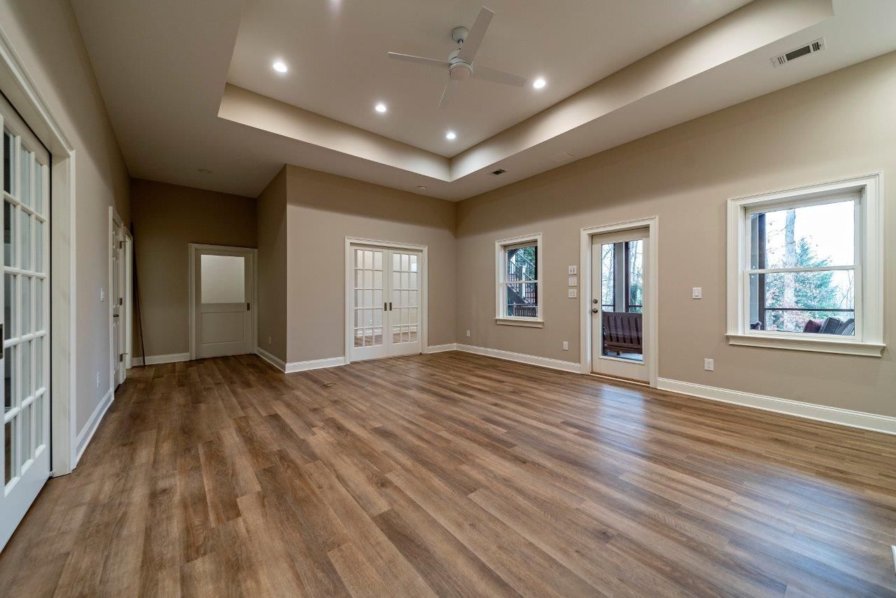 Empty room with hardwood floors, beige walls, and a recessed ceiling. Two doors, two windows.