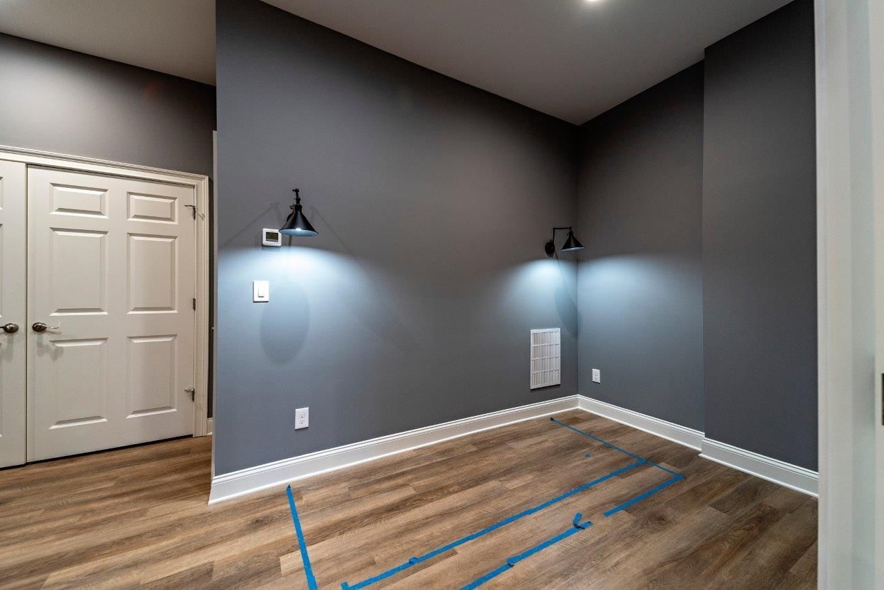 Empty room with gray walls, wood-look floor, white trim and doors, two black sconces, and blue tape.