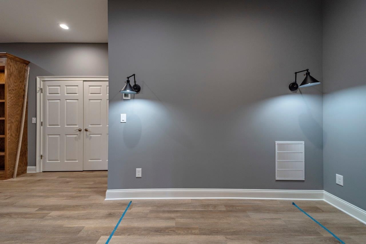 Gray wall with sconce lighting, white trim, two doors, and light wood-look flooring.