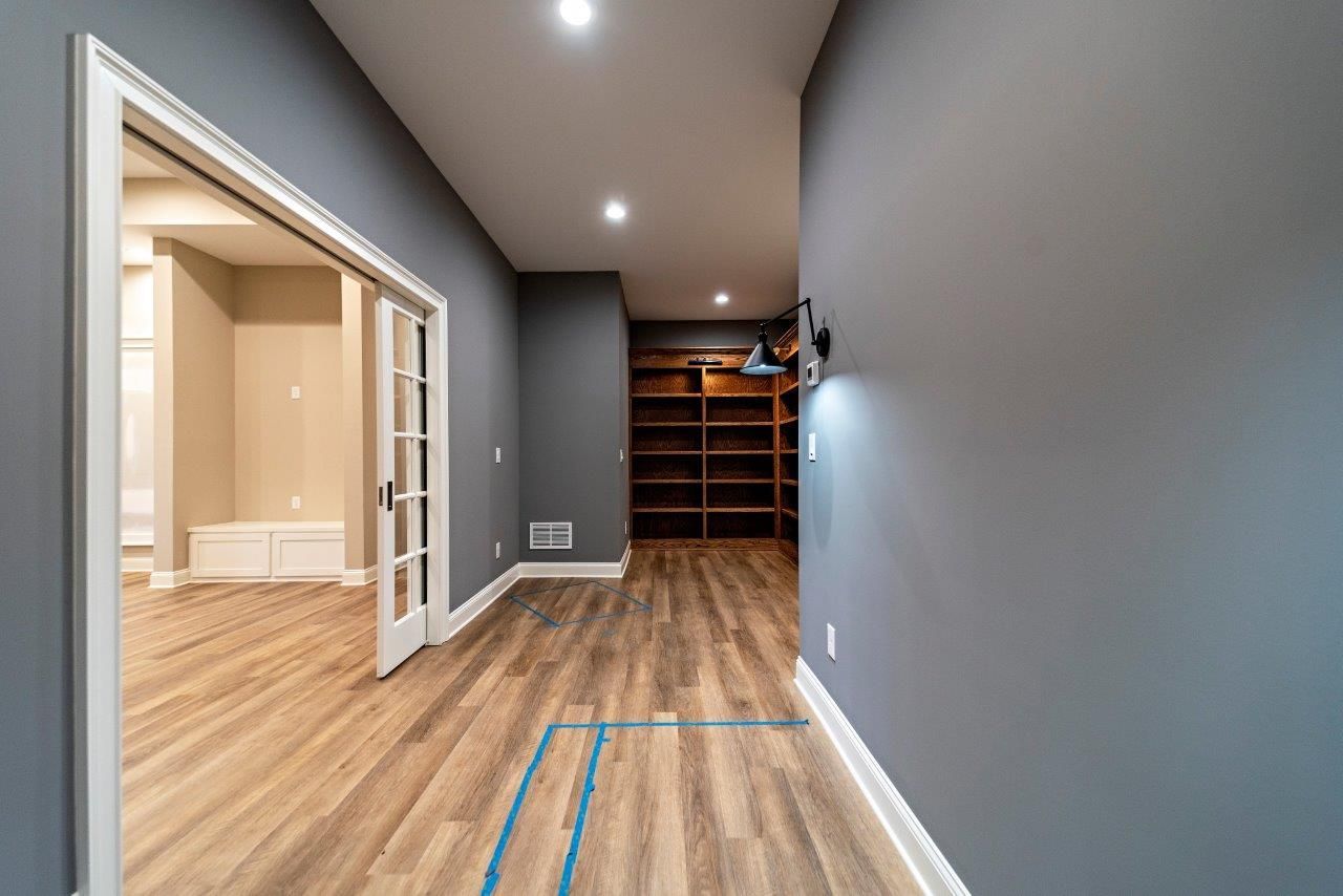 Long hallway with wooden floors, gray walls, and built-in bookshelves. A doorway leads to another room.