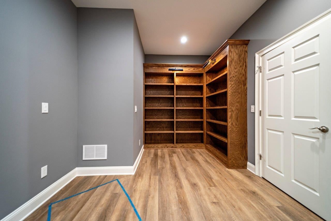 A room with gray walls, wood-look floor, built-in wooden bookshelves, and a white door.