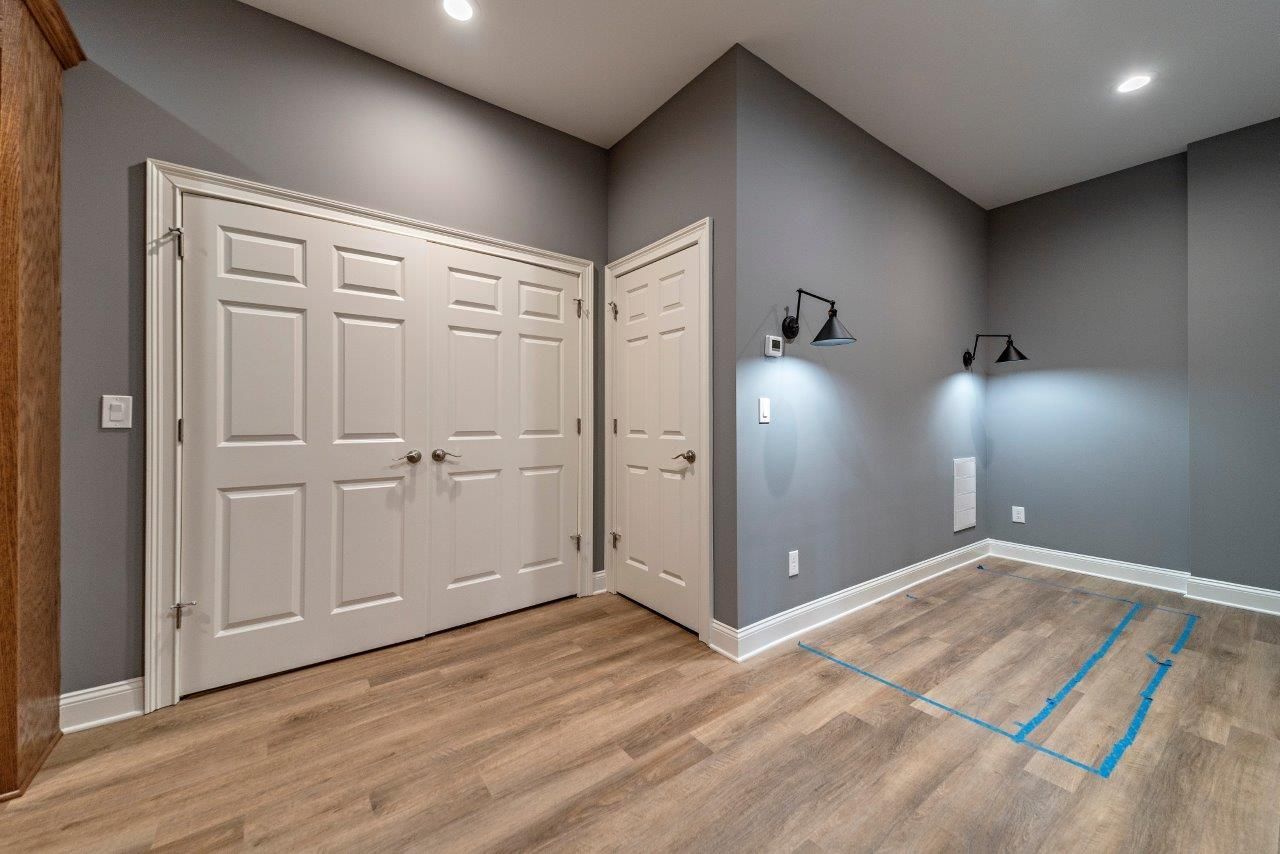 Gray-painted room with white doors and wood-look flooring. Two wall sconces illuminate a section of the wall.